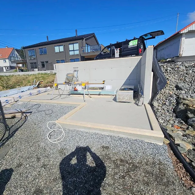 Ny støpt betongplate og støttemur under bygging i boligområde med hus og fjordutsikt i bakgrunnen.