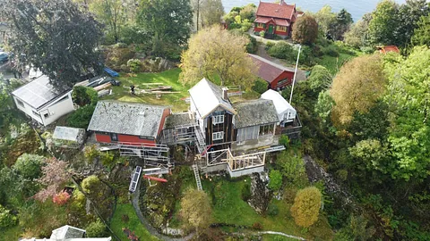 Luftfoto av bolig under rehabilitering med stillas, tilbygg og frodig hage rundt eiendommen.