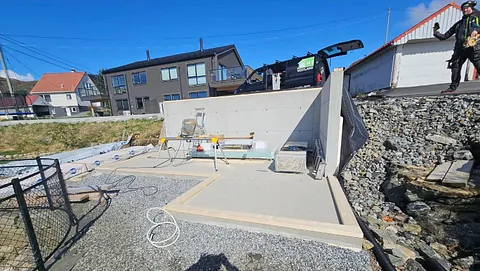 Støttemur og ny støpt betongplate under bygging i boligområde med hus i bakgrunnen.